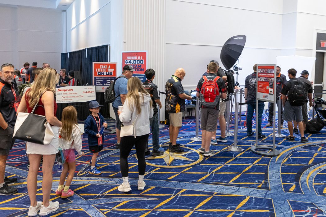 Attendees queuing behind stanchions at a HeadshotDC headshot station inside a sponsor's trade show booth, with branded signage and studio lighting