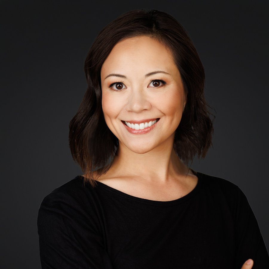 Portrait of a woman with shoulder-length dark hair smiling against a black background.